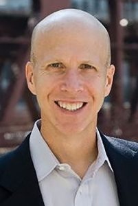 A bald man smiles into the camera