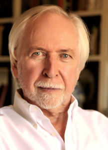A man with white hair and a beard stares into the camera