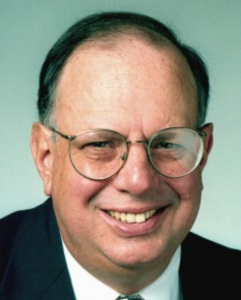 A man with glasses smiles into the camera