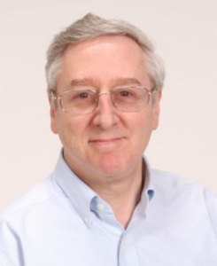 A man with glasses and gray hair looks into the camera
