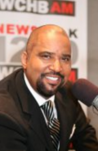 A bald man smiles behind a microphone