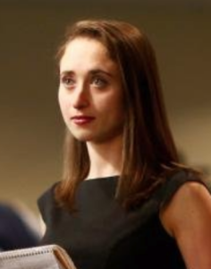 A woman with brown hair and a black blouse looks off into the distance