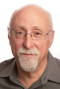 A man with glasses and a gray beard looks into the camera