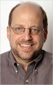A man with glasses smiles into the camera