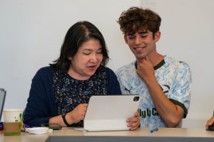 Two people look at a computer, smiling.