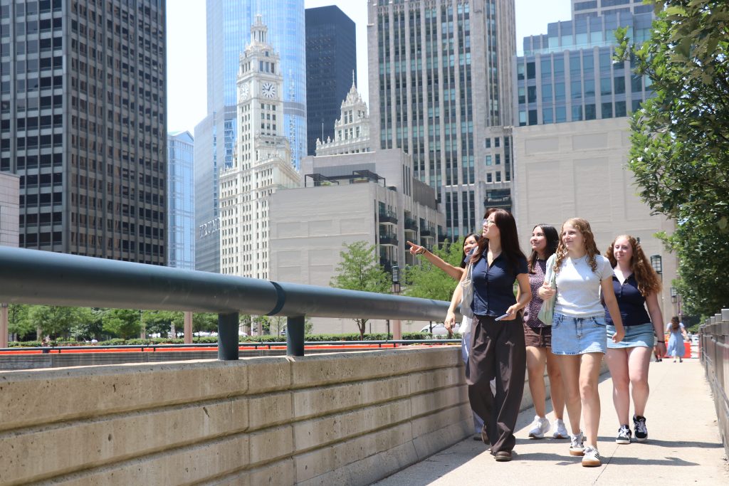 Five people walk across a bridge. One is pointing to the left as the others look in the same direction.