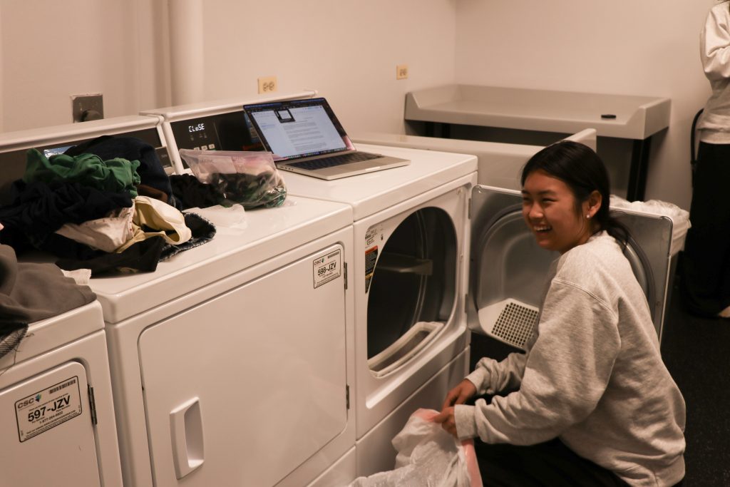 A person crouches by a washing machine to switch their laundry.