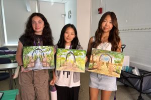 Three people stand while holding canvases.