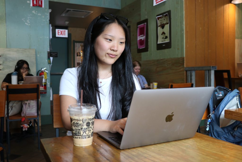 A person types on their computer with a coffee cup.