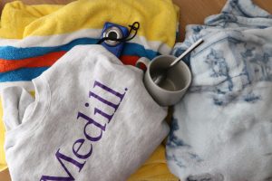 Some blankets, a sweatshirt, a mug and a camera sit on the floor.