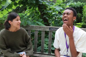 Two people sit on a bench. The person on the right is laughing.
