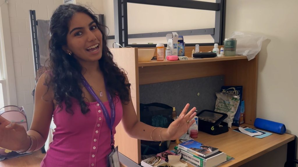 A person stands in front of their dorm room desk.